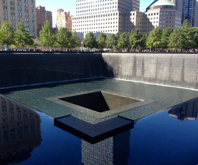 The North Pool at the National September 11 Memorial in lower Manhattan, its waterfalls framed by the surrounding city skyline.